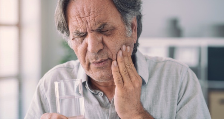 Older man with tooth pain holding a glass of water — when to see an emergency dentist