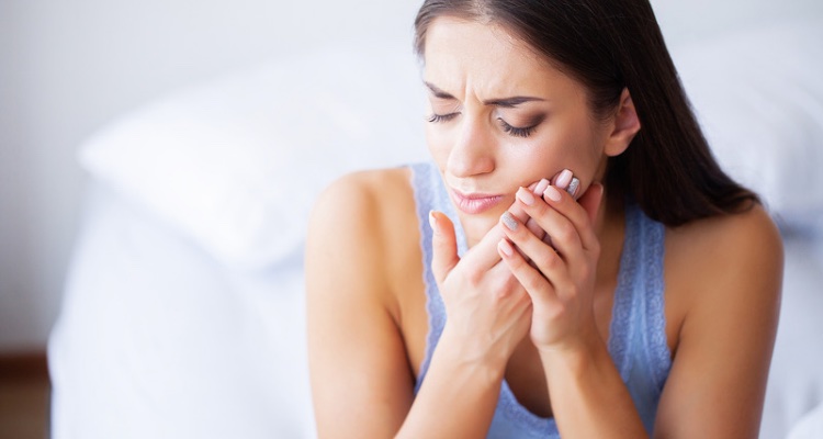 Woman with a toothache holding her jaw — signs of a dental emergency